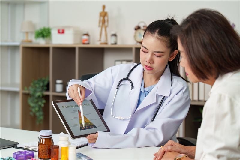 A physician sitting beside a patient, explaining health information on a tablet